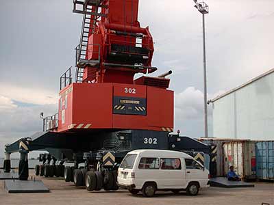 a little white van in front of a port crane in sihanoukville